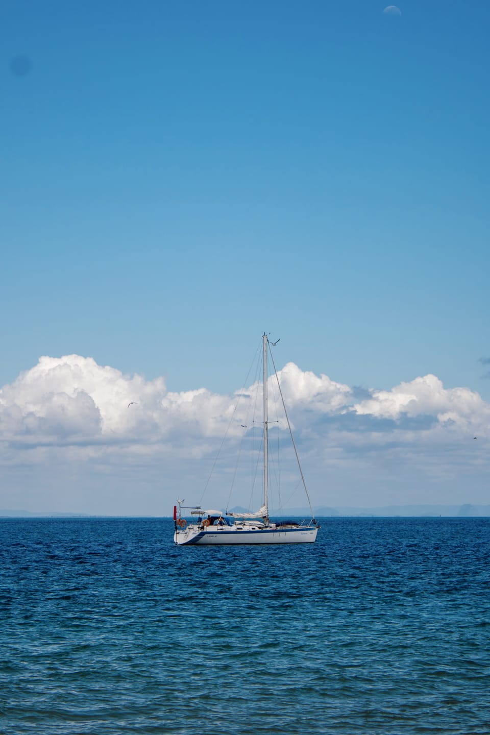 A white sailing yacht at anchor on calm blue water, with a bank of cumulus clouds along the horizon